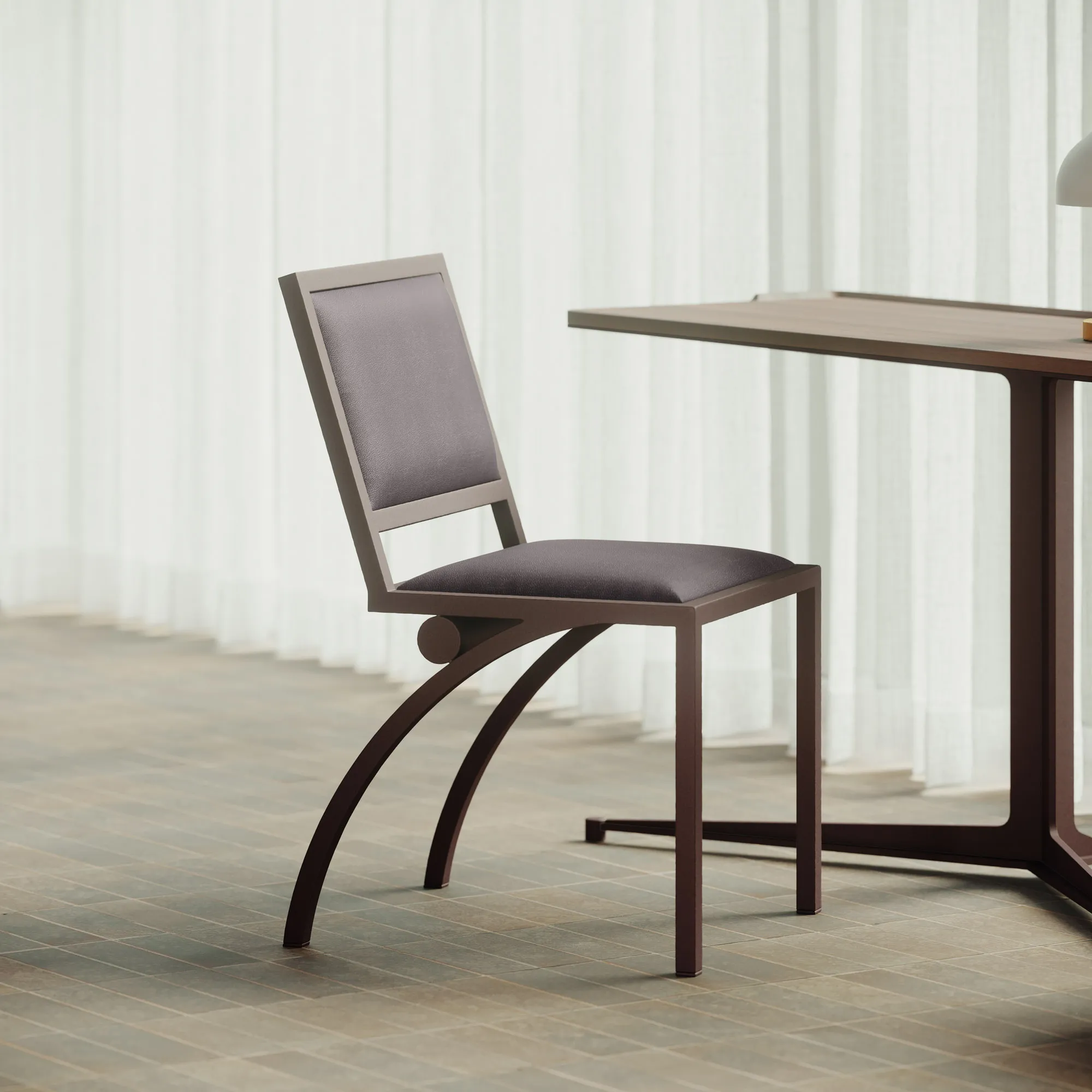 Cylindre chair in satin bronze and dark leather beside a table in a softly lit interior
