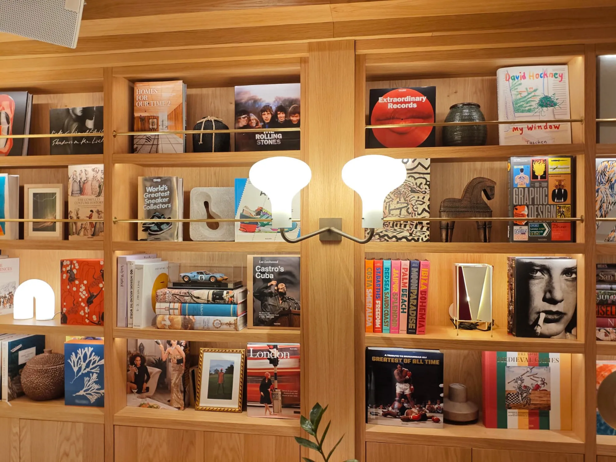 Two-shade wall lamp set among books and objects on wooden shelves at Brown’s Avenue Hotel
