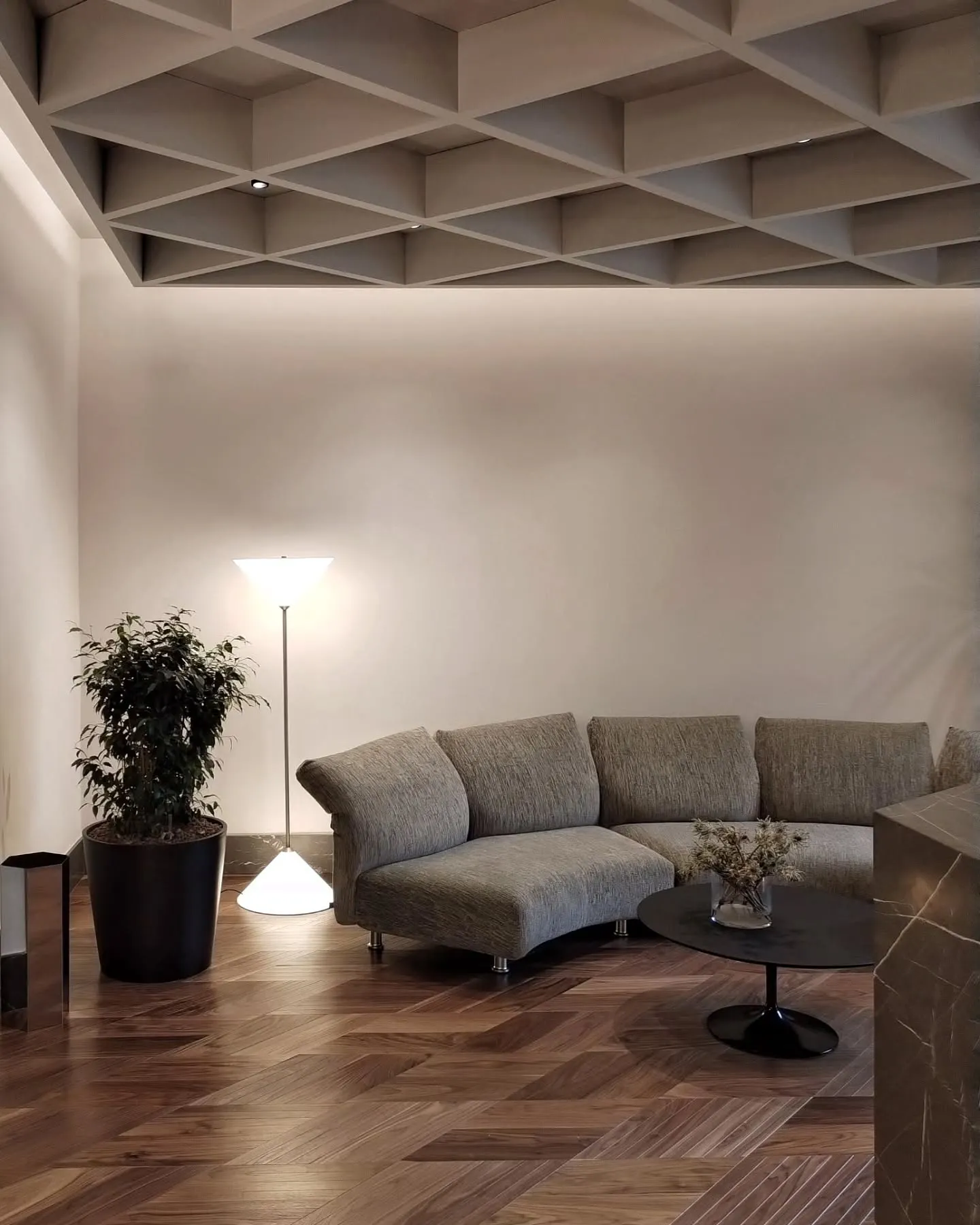 Pale sofa and floor lamp beneath the geometric ceiling of the Milan office lounge