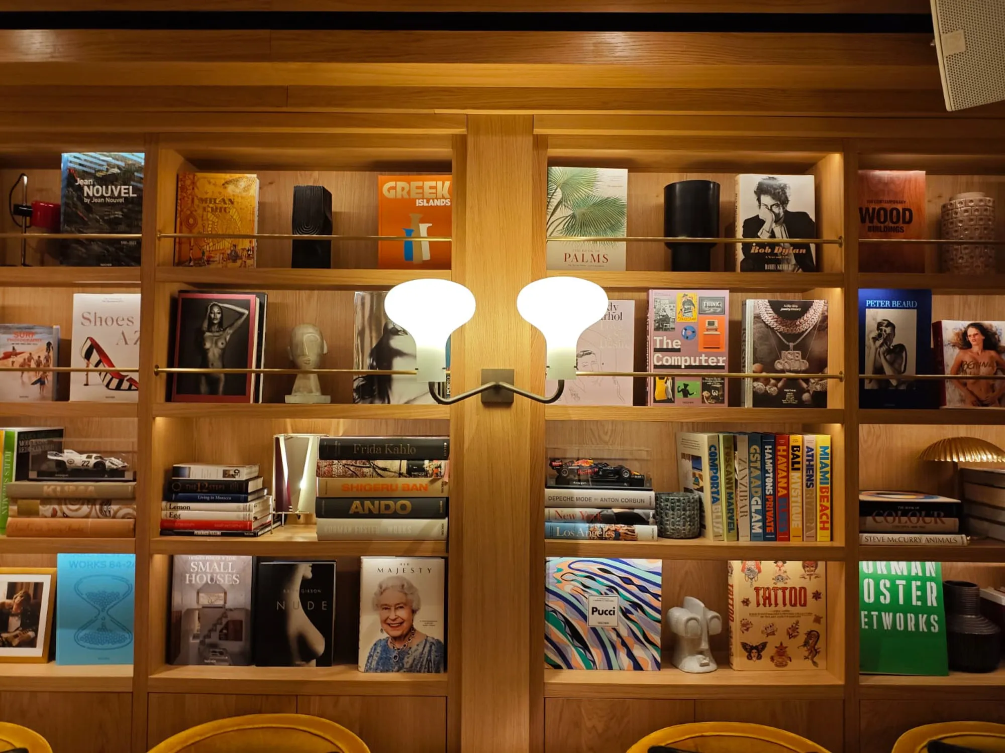 Front view of a white glass wall lamp between illuminated bookshelves in the hotel lounge