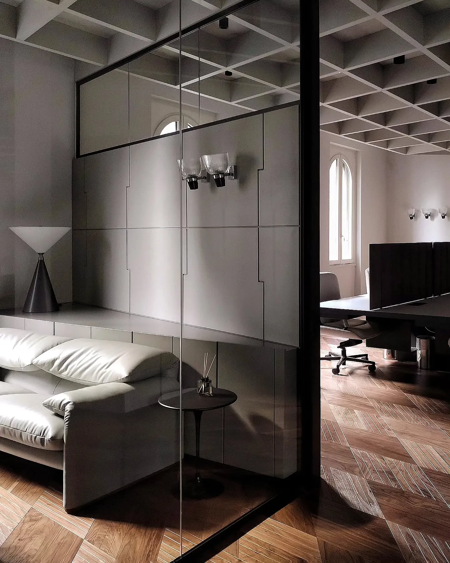 Glass-partitioned office room with a pale sofa and herringbone timber floor