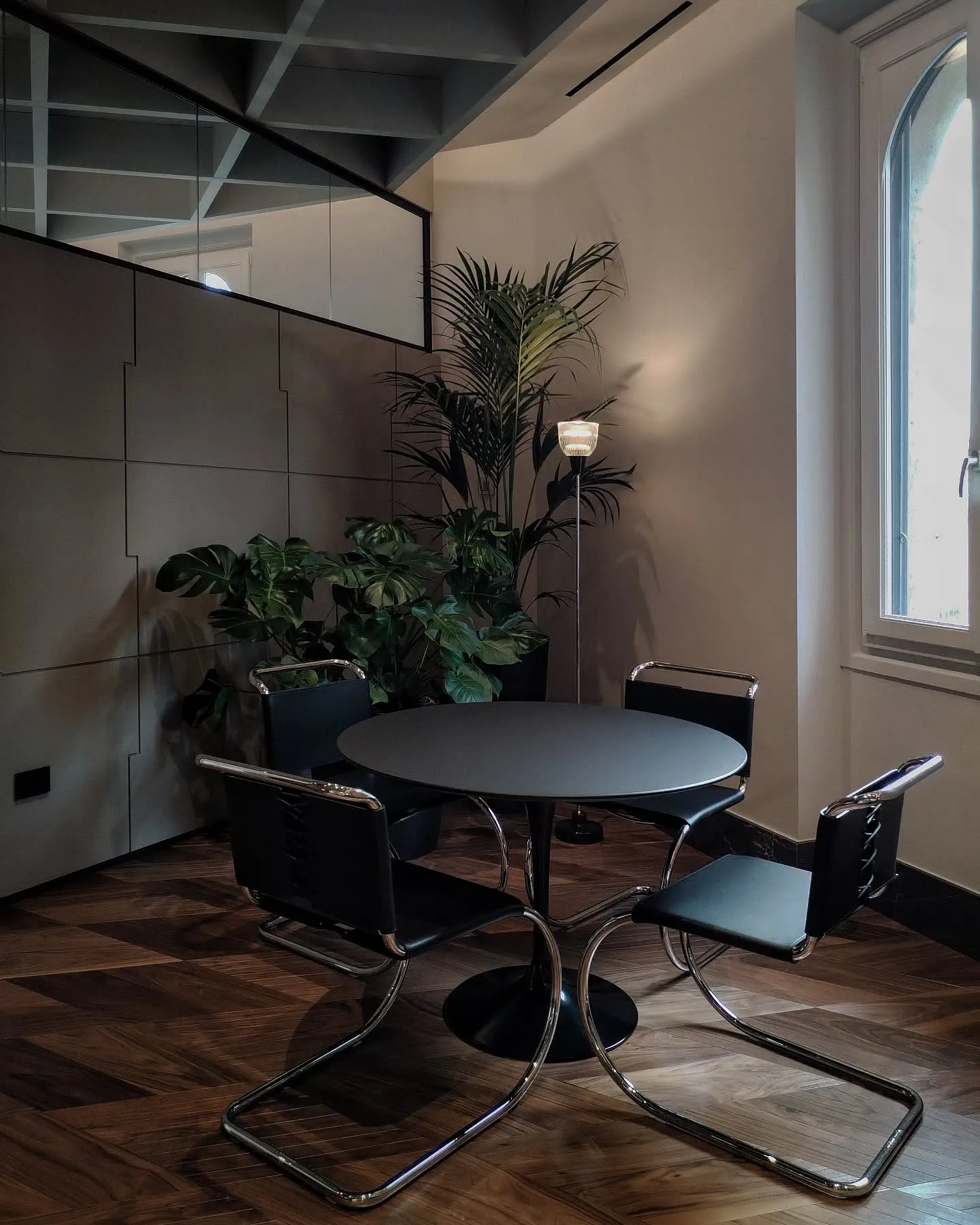 Small round meeting table, chairs and greenery beside an arched window in the Milan offices