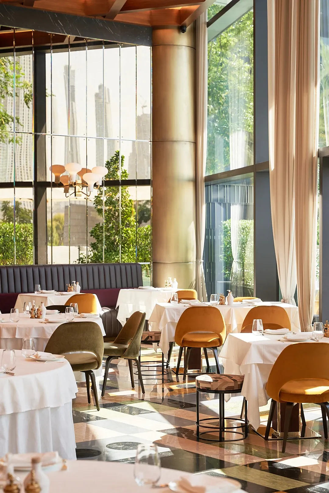 Daylit dining room at The Arts Club Dubai with tall windows and upholstered chairs