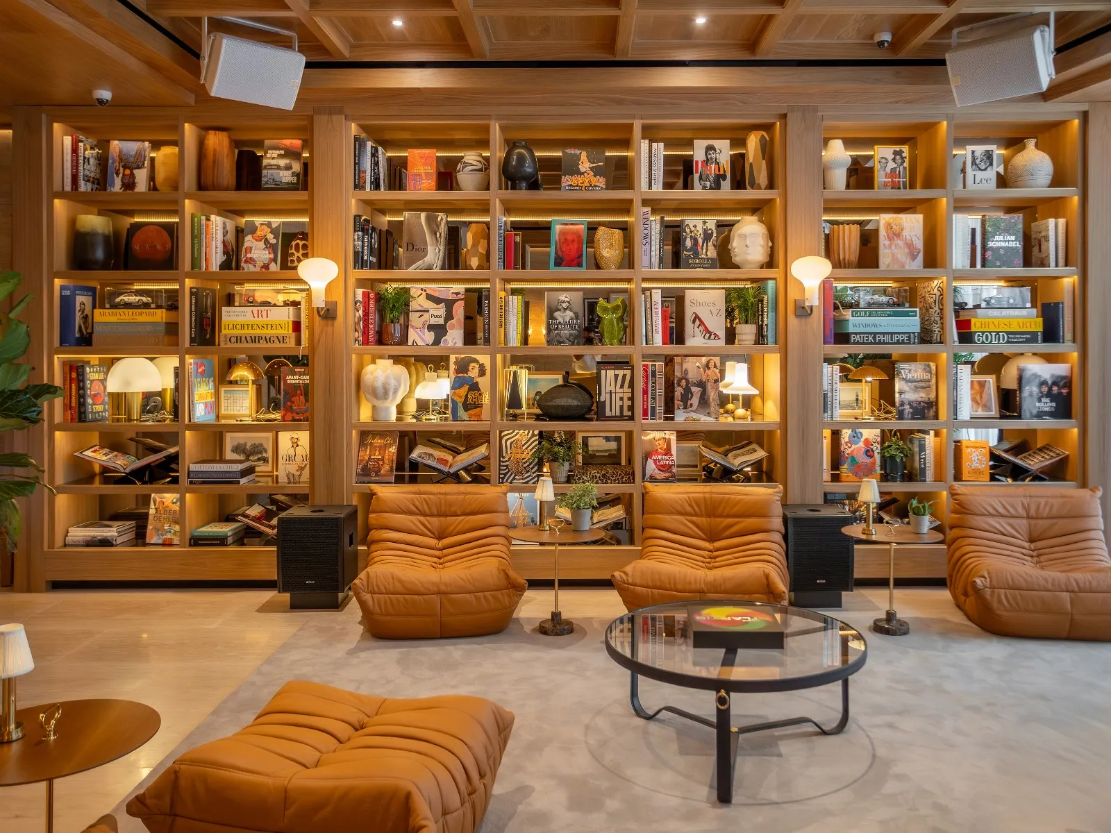 Library seating area with ochre chairs, a round coffee table and lamps beside the bookshelves