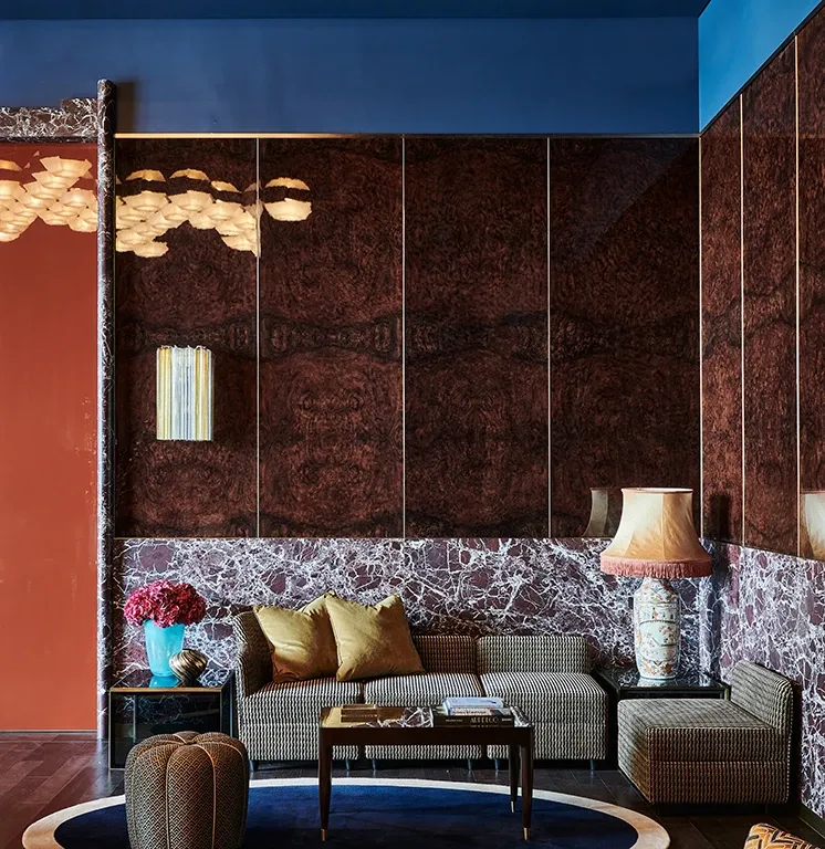 Intimate lounge at The Arts Club Dubai with dark red walls, a patterned sofa and table lamp