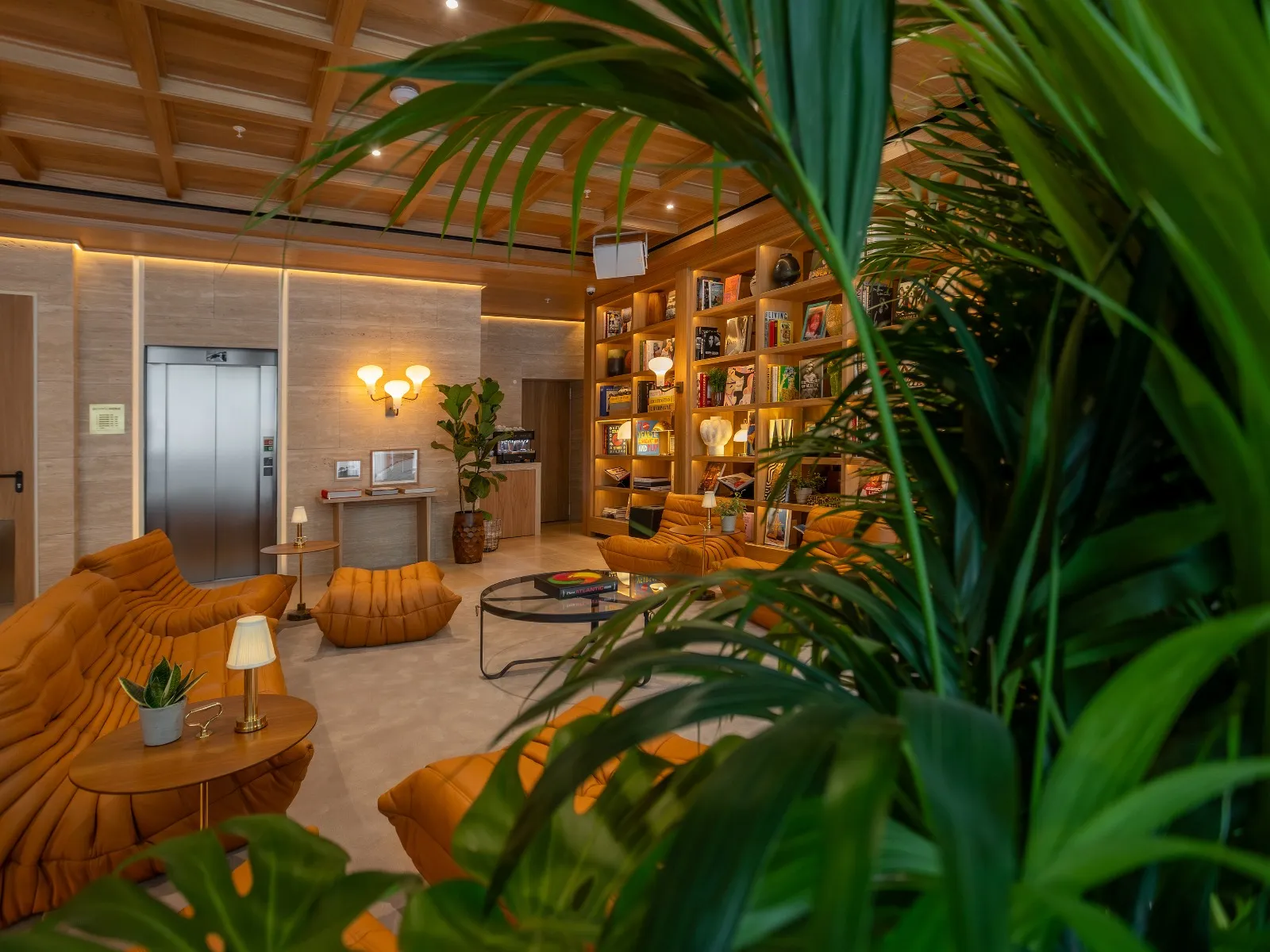 Hotel lounge seen past a large indoor plant, with upholstered seating and wooden shelving