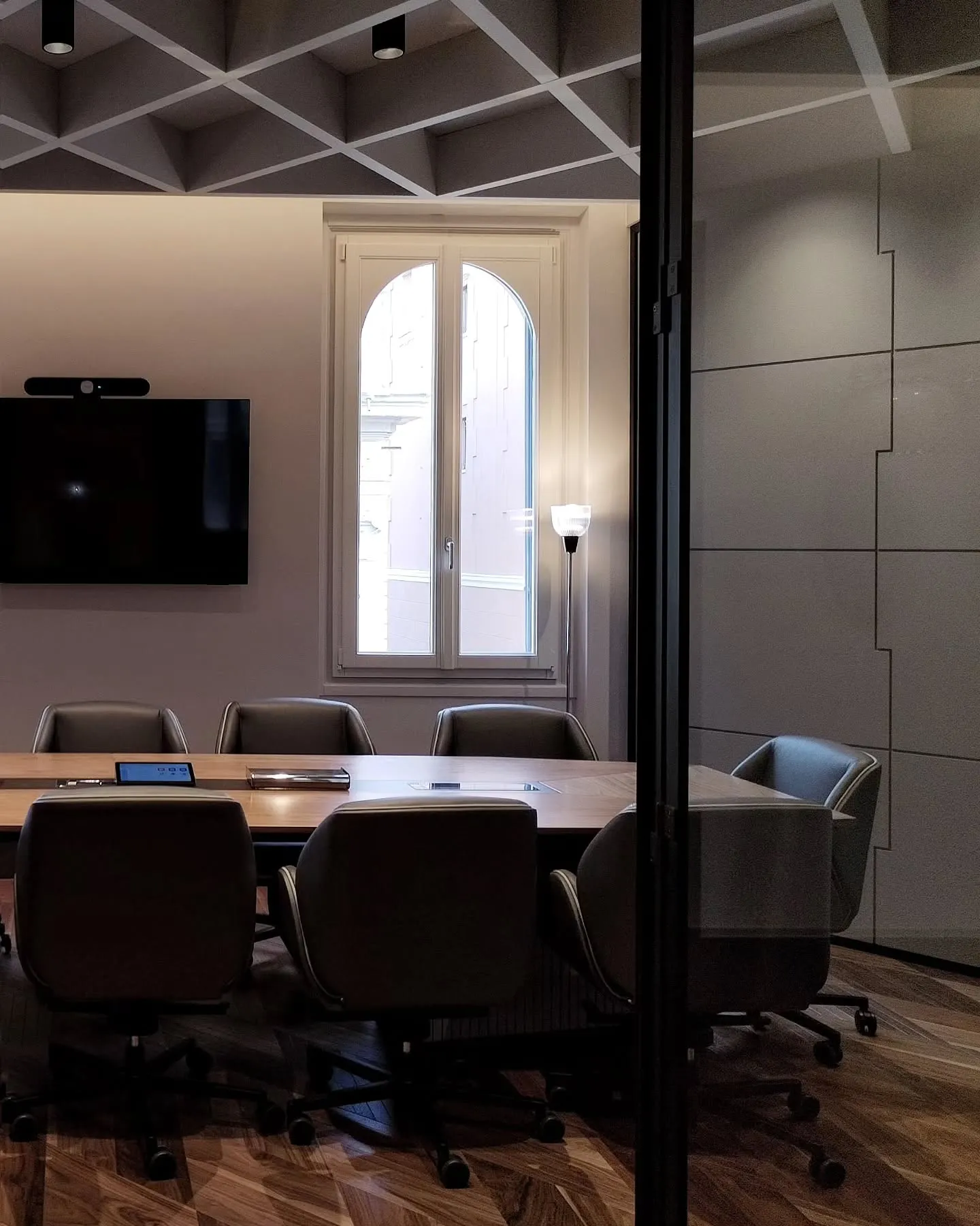 Office meeting room with dark chairs, a desk and an arched window beyond glass partitions