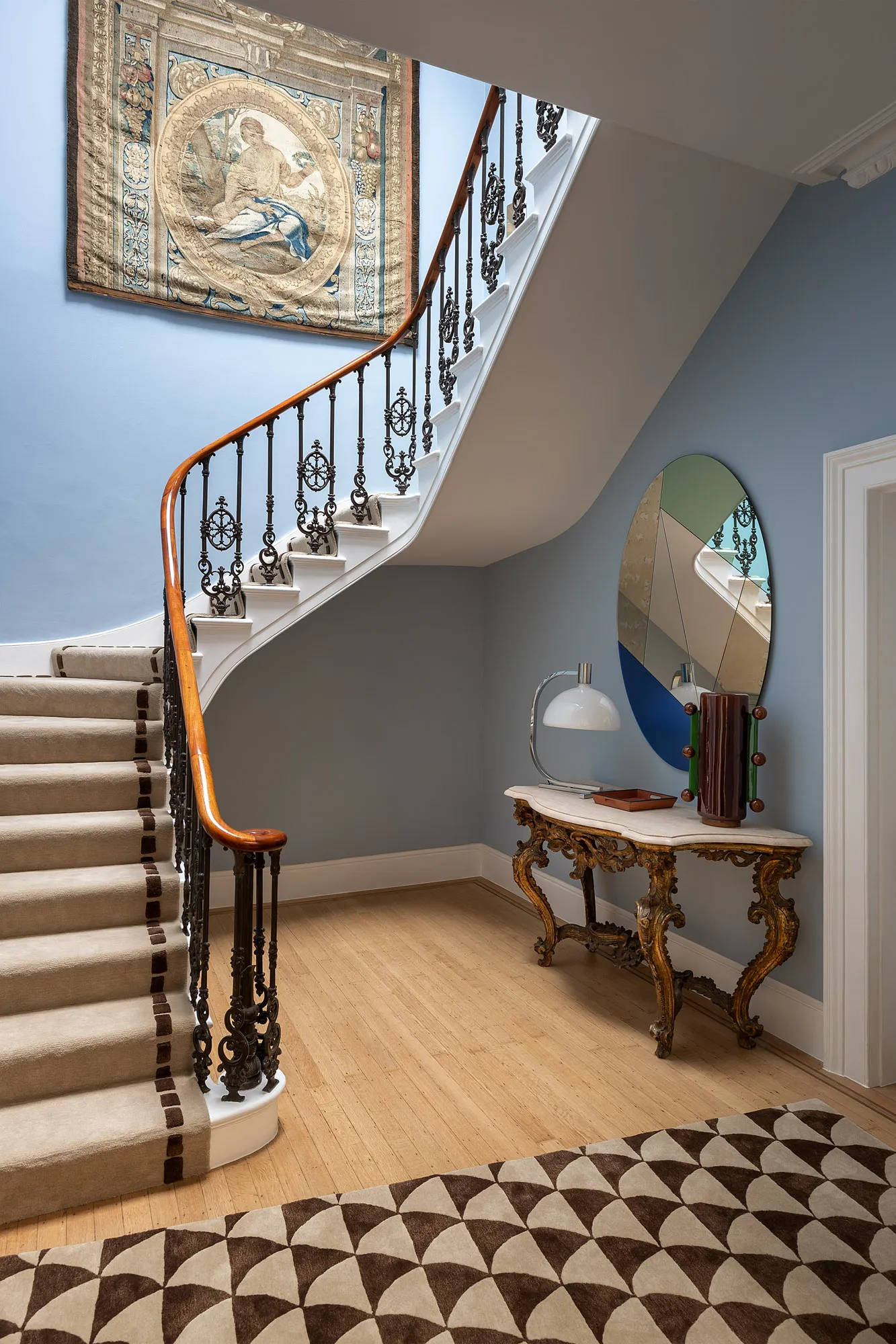 Curving staircase with an antique railing, console table and round mirror