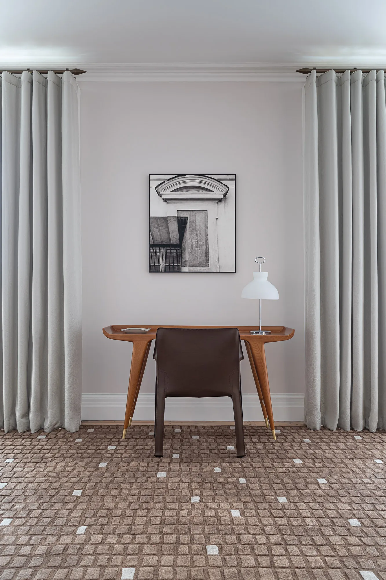 Small timber desk and white table lamp in front of full-height curtains