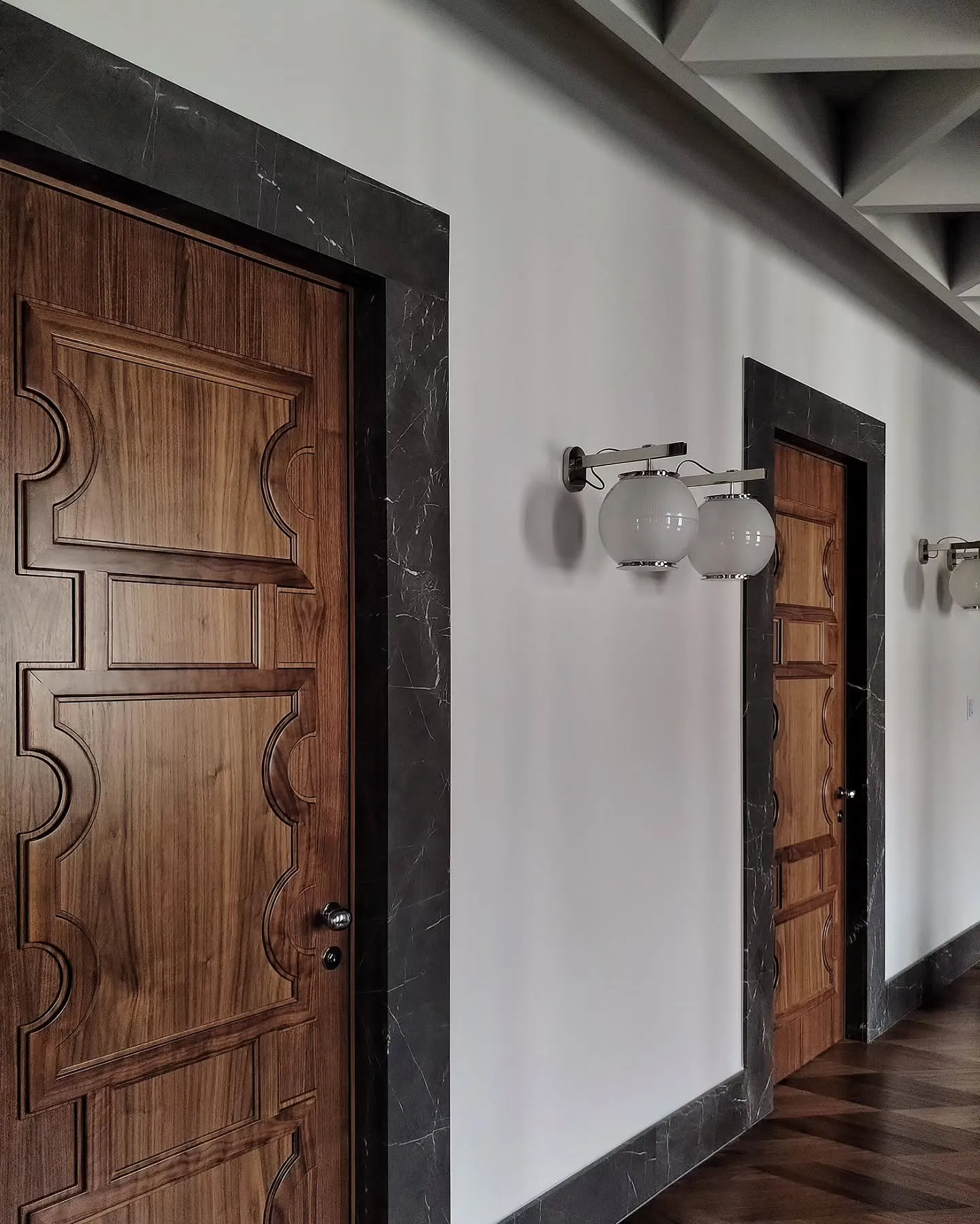 Carved timber doors and a pair of glass wall lamps in the Milan office corridor