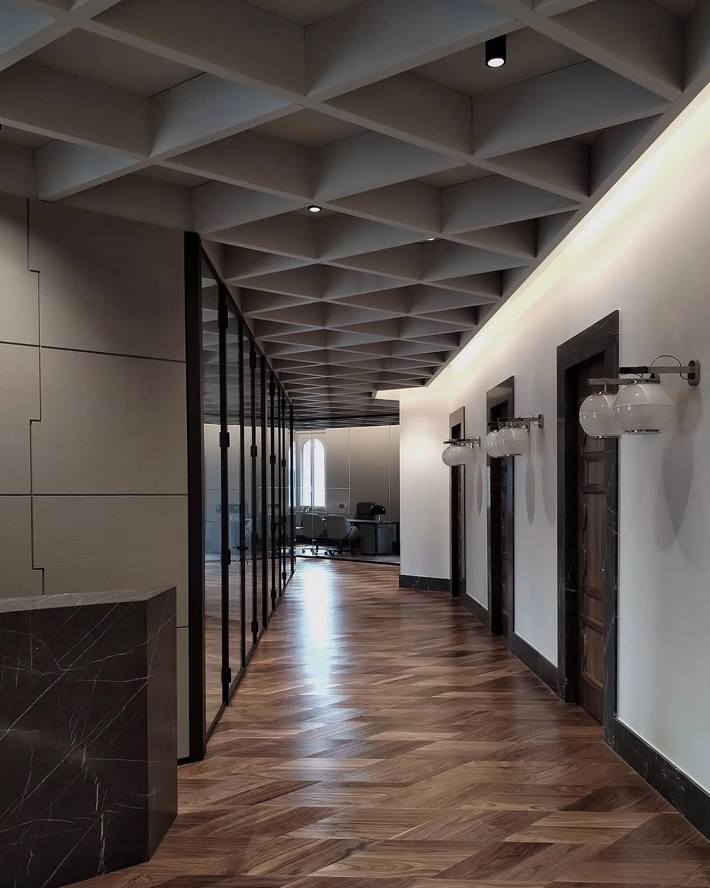 Long office corridor with glass partitions, wall lamps and herringbone timber flooring