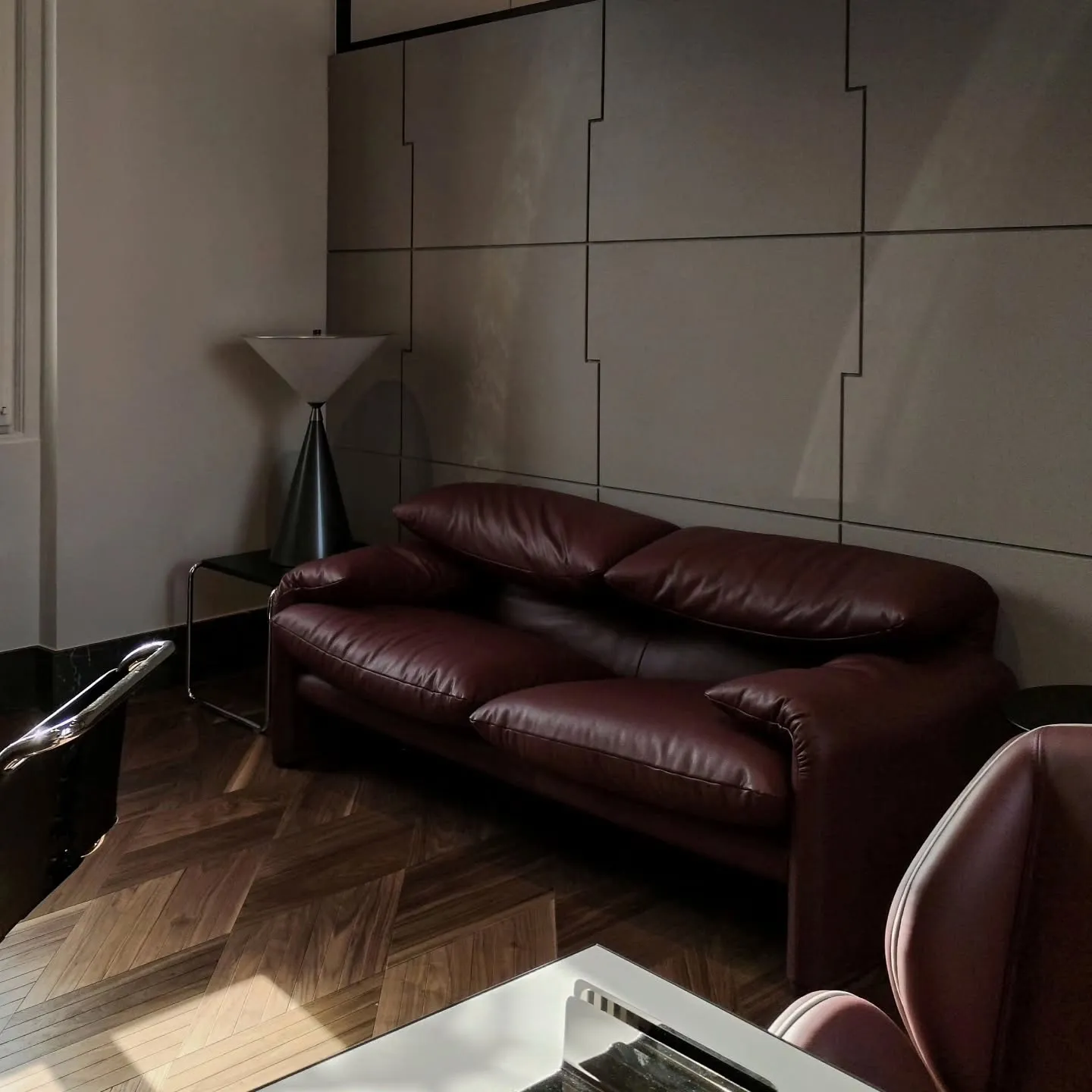 Burgundy leather sofa and sculptural floor lamp against a panelled office wall